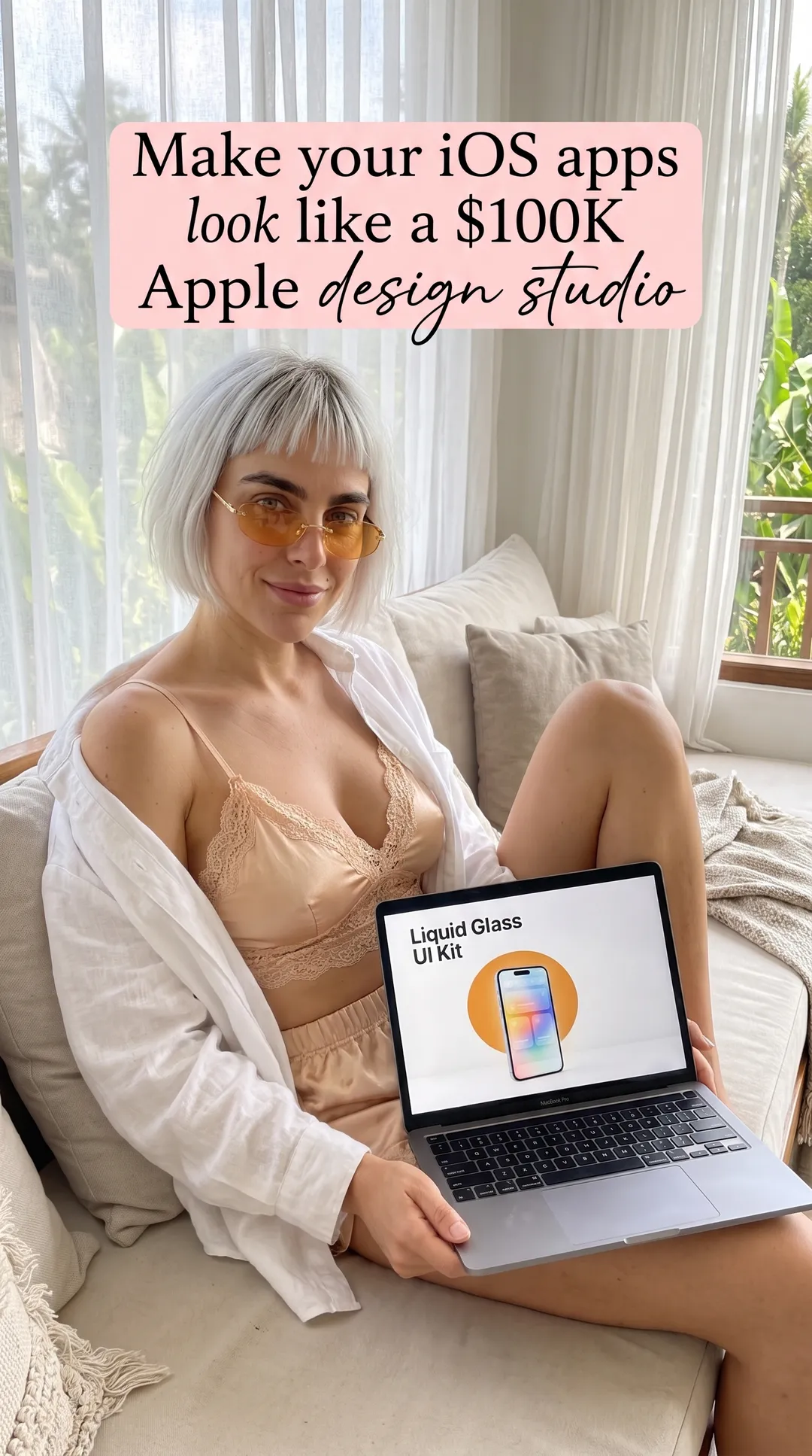 Kaia in a beige satin cami and open white shirt on a daybed with a laptop showing the iOS 26 Liquid Glass UI Kit