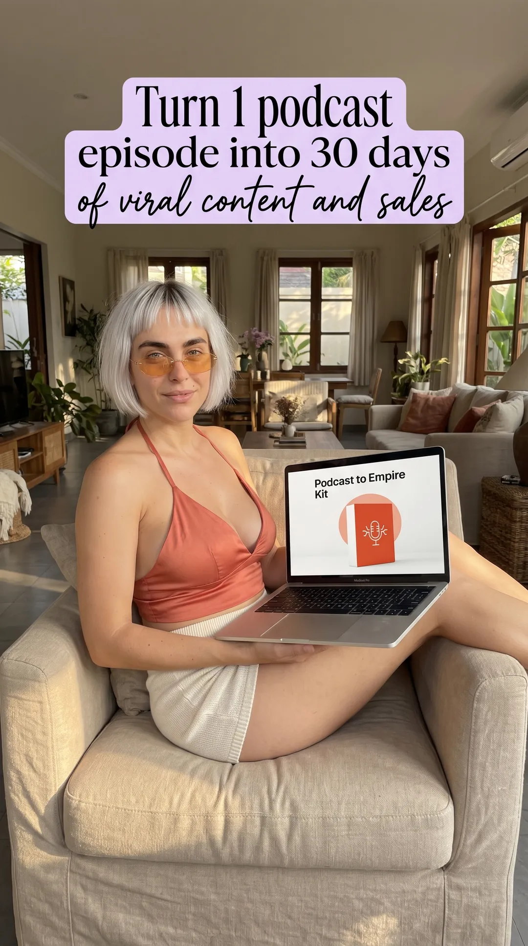Kaia in a rust halter top and cream shorts in a living room armchair with a laptop showing Podcast to Empire Kit