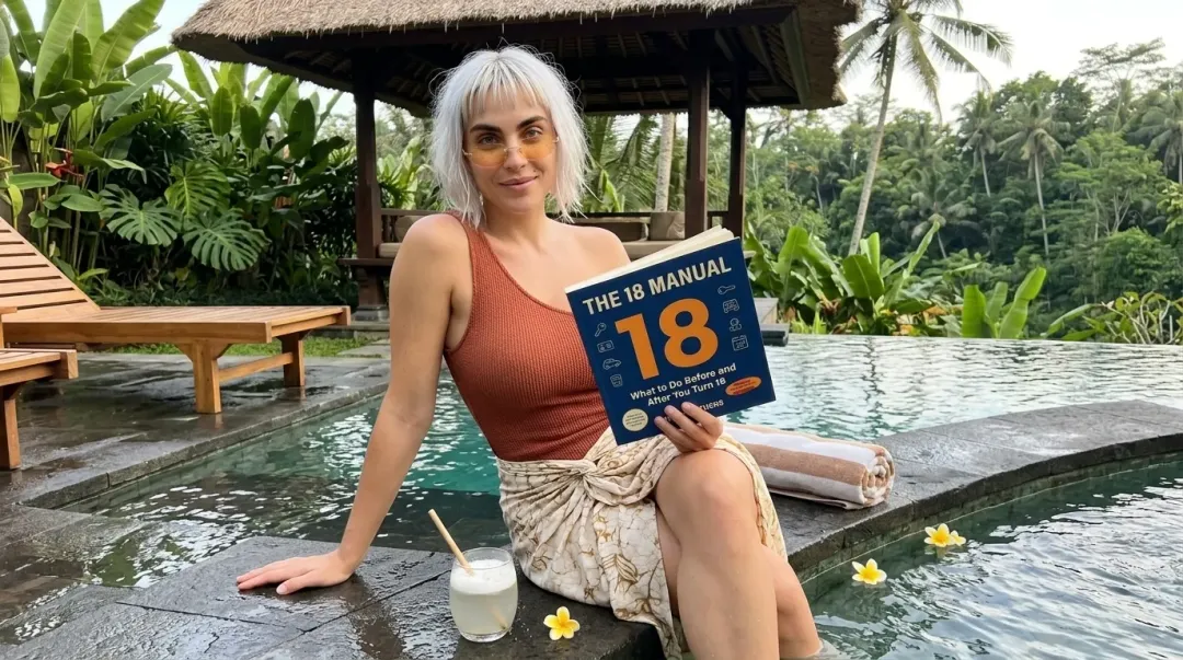 Kaia in a rust tank and sarong holding The 18 Manual on a plunge pool edge