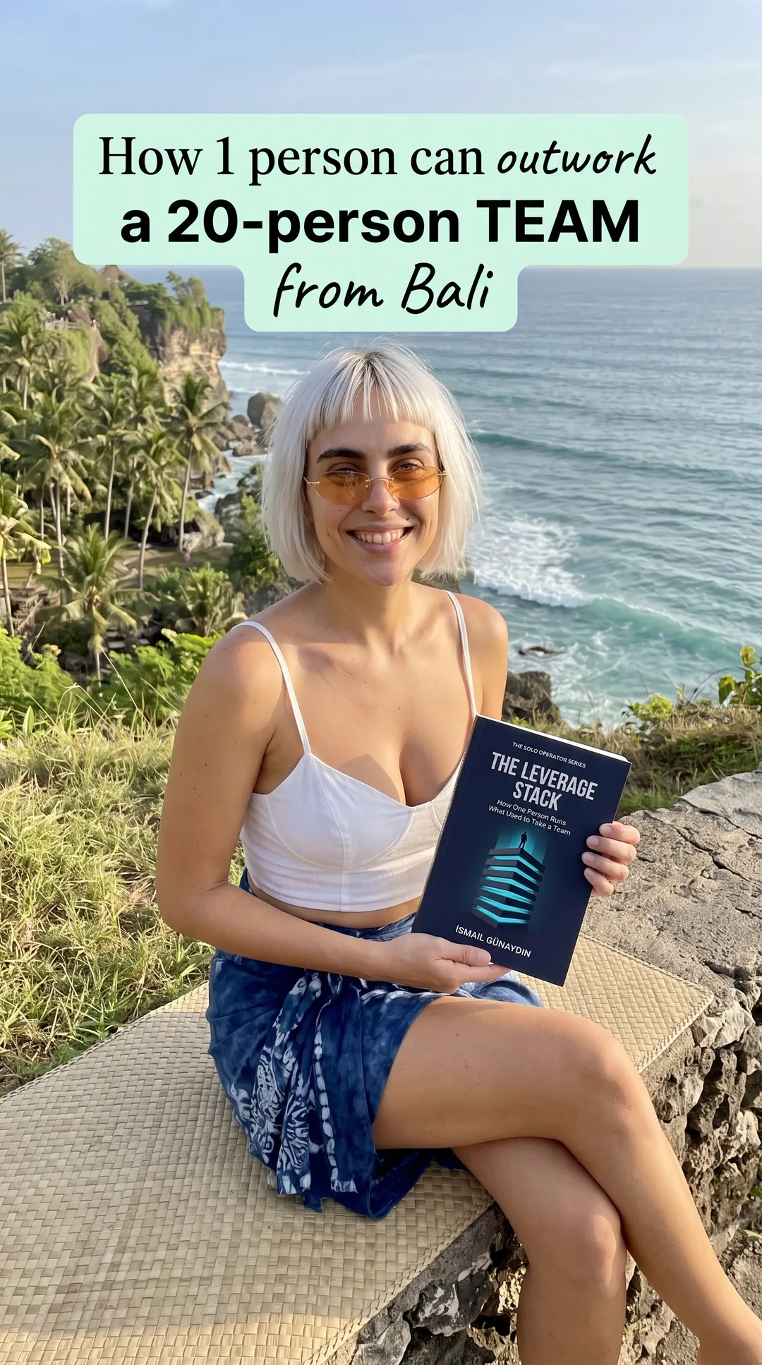 Kaia in a white cami and blue skirt on a seaside cliff holding The Leverage Stack