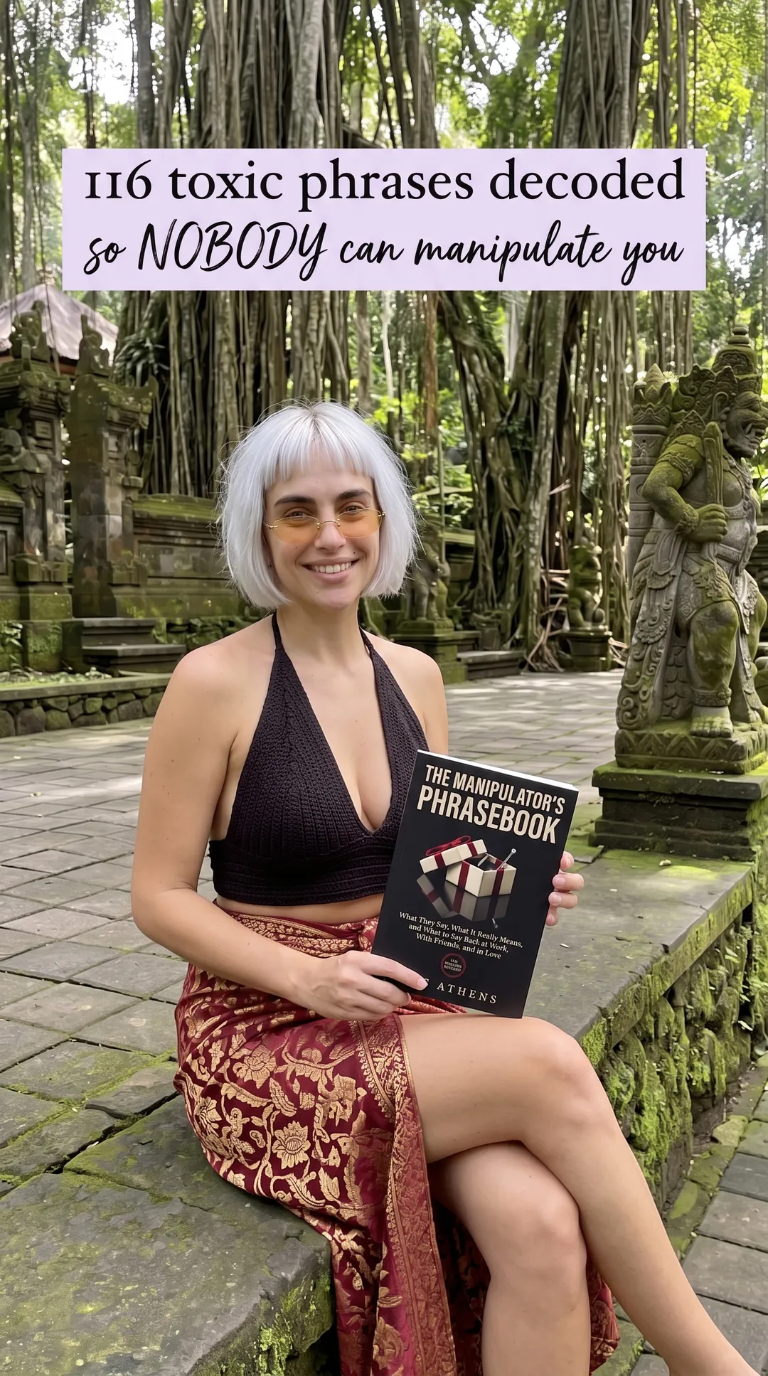 Kaia in a black halter and red sarong at a temple courtyard holding The Manipulator's Phrasebook