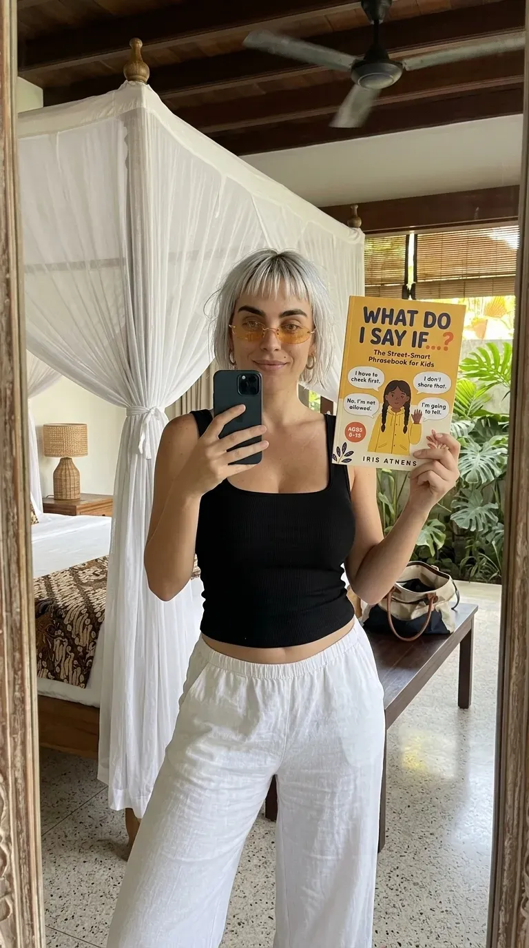Kaia in a black tank and linen pants holding What Do I Say If...? in a mirror selfie